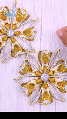 two gold and white flower brooches sitting on top of a wooden table