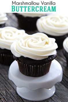 chocolate cupcakes with white frosting sitting on top of a cake stand and the words marshmallow vanilla buttercream above them