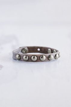 The Dotty stacker bracelet is handmade from lamb leather and features a row of brushed silver domed rivets. **Contents** * Lambskin leather, zinc alloy hardware * Button clasp closure * Handmade **Care/Import** * Made in the USA **Dimensions** * Adjustable to fit wrist sizes 6.5”-8” | Giving Bracelets Brushed Silver Dotty Leather Bracelet at Free People in Grey Adjustable Metal Bracelets With Studs, Silver Leather Bracelets With Studs, Silver Leather Jewelry With Studs, Adjustable Silver Leather Bracelet With Rivets, Metal Bracelets With Rivets For Gift, Metal Rivets Bracelets As Gift, Adjustable Vintage Leather Bracelet With Rivets, Vintage Adjustable Leather Bracelet With Rivets, Vintage Leather Bracelets With Rivets