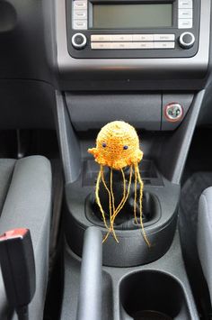 a stuffed animal sitting in the center console of a car, wearing a yellow knitted hat