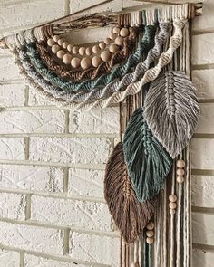 a wall hanging made out of yarn and wood beads with leaves on the top, attached to a brick wall