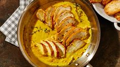 a pan filled with food next to bread on top of a wooden table and a checkered cloth