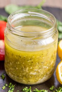 a glass jar filled with pesto sauce next to sliced lemons and tomatoes