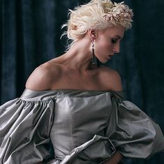 a woman with blonde hair wearing an off the shoulder silver dress and holding her hand on her hip