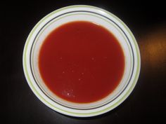 a white bowl filled with red liquid sitting on top of a wooden table next to a black wall