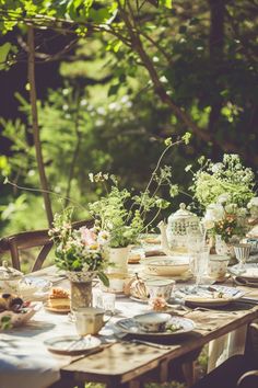 the table is set with plates, cups and vases full of flowers on it