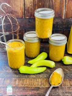 several jars filled with yellow colored food sitting on top of a wooden table next to spoons