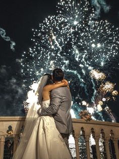 a bride and groom kissing in front of fireworks at their wedding reception, taken from the balcony