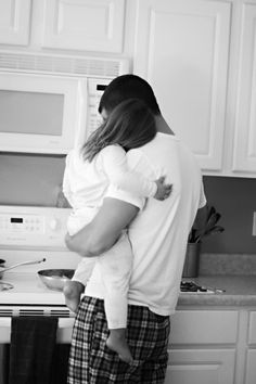 a woman holding a baby in her arms while standing next to a stove top oven