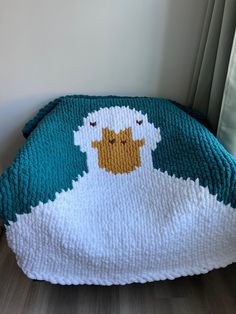 a crocheted sheep blanket sitting on top of a wooden floor next to a window