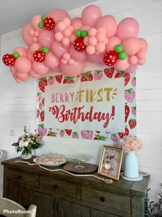 a birthday party with pink and green balloons hanging from the ceiling over a buffet table