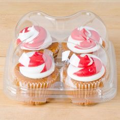 two cupcakes with red and white frosting in a plastic container on a wooden table