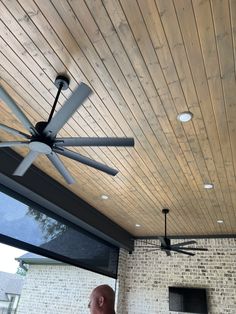 a man standing under a ceiling fan in front of a brick wall and patio area