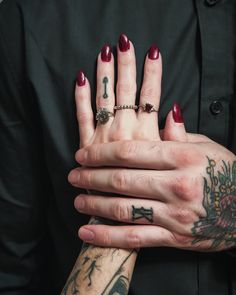 a woman's hands with tattoos and rings on her left wrist, holding onto the other hand