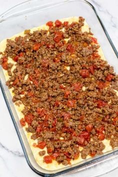 an uncooked casserole dish with meat and tomato toppings on top