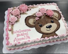 a birthday cake decorated with a teddy bear and pink flowers on the top, says welcome baby america