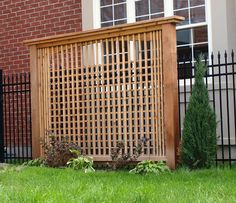 a wooden trellis in front of a brick building with green grass and bushes next to it