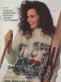 a woman holding two skis and wearing a sweater with an image of trees on it