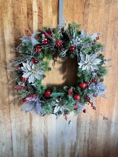 a christmas wreath hanging on the side of a wooden door with red berries and silver leaves