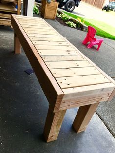 a wooden bench sitting on top of a cement floor next to a pink chair and tree