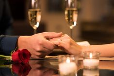 two people holding hands over a table with candles and roses on it, while one holds the hand of another person's hand