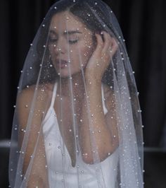 a woman wearing a wedding veil and holding her hand to her face with rain drops on it