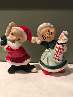 two santa claus figurines sitting on top of a counter next to each other