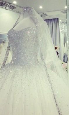 a white wedding dress with silver sequins on the bouncy skirt is displayed in front of a mirror