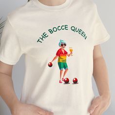 "This Bocce Shirt sports a colorful rendition of \"The Bocce Queen\".  She's ready to play, or party, or both. This classic unisex jersey short sleeve tee fits like a well-loved favorite. Soft cotton and quality print make users fall in love with it over and over again. These t-shirts have-ribbed knit collars to bolster shaping. The shoulders have taping for better fit over time. Dual side seams hold the garment's shape for longer.  .: 100% Airlume combed and ringspun cotton (fiber content may v Bocce Party Ideas, Bocce Ball Team Shirts, Bocce Ball Set, Bocce Ball, Puppy Valentines, Pickleball Sports Season Graphic T-shirt, Balls Shirt, Team Shirts, Team Gifts