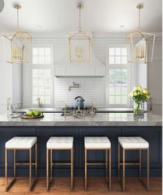 a kitchen island with four stools in front of it and three lights hanging from the ceiling