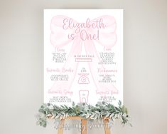 a pink and white wedding sign with greenery on the bottom, in front of an easel