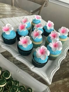 cupcakes with blue frosting and pink flowers on them sitting on a plate