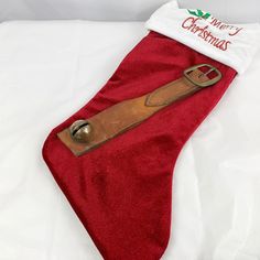 a red christmas stocking with a bell on it sitting on a white bed sheet