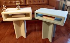 two side tables sitting on top of a hard wood floor next to a brown couch