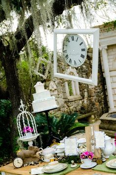 a table topped with lots of plates covered in cake next to a clock and birdcage