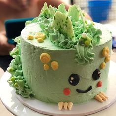 a cake decorated with green frosting and flowers on a plate next to a person's hand