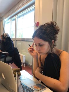 a woman sitting in front of a laptop computer while holding a pen and looking at the screen