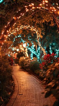 an archway with lights on it is lit up in the night time, and surrounded by greenery