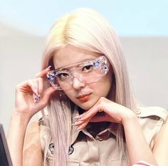 a woman wearing glasses sitting at a table in front of a laptop computer and holding her hand to her face