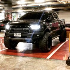 a black truck is parked in a parking garage with other cars behind it and on the ground