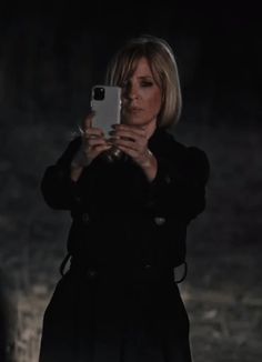 a woman taking a selfie with her cell phone in the dark, while wearing a black coat