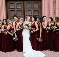 a group of women standing next to each other in front of a door holding bouquets