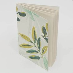 an open book with yellow and green leaves on the cover, sitting on a white surface