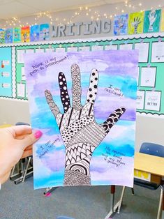 a person holding up a piece of art in front of a classroom wall with writing on it