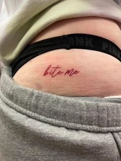 a woman's lower back tattoo with the word bite me written on her right side