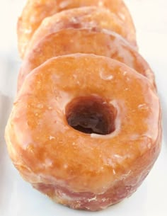 four glazed donuts sitting on top of a white plate