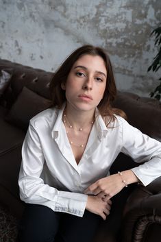 a woman sitting on top of a brown couch wearing a white shirt and black pants