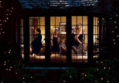 three women are seen through the window of a house at night with christmas lights all around them