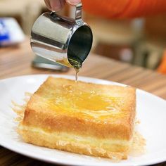 a person pouring syrup on top of a piece of bread that is sitting on a white plate