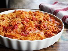 a casserole dish filled with spaghetti and tomato sauce on a wooden table next to a towel